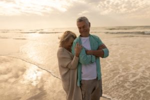 front view of active senior woman embracing senior woman on the beach at dusk